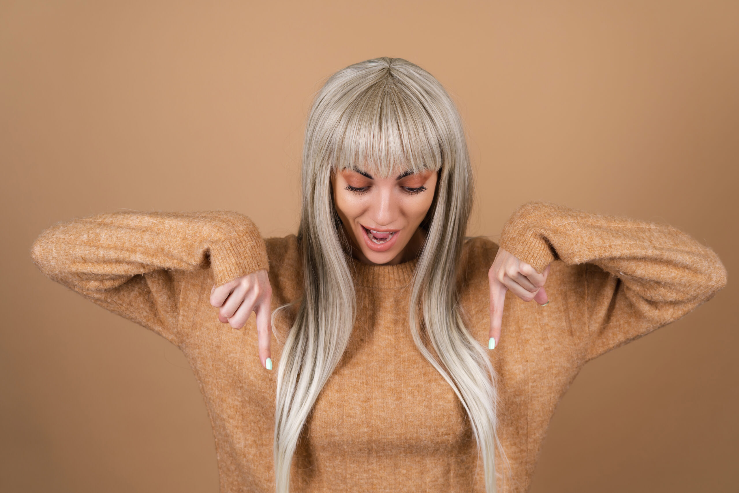 Blonde girl with bangs and brown daytime makeup in a sweater on a beige background smiles excitedly points her finger down 20 Inch Clip-in Streaks – Vibrant Length & Volume - Image 1